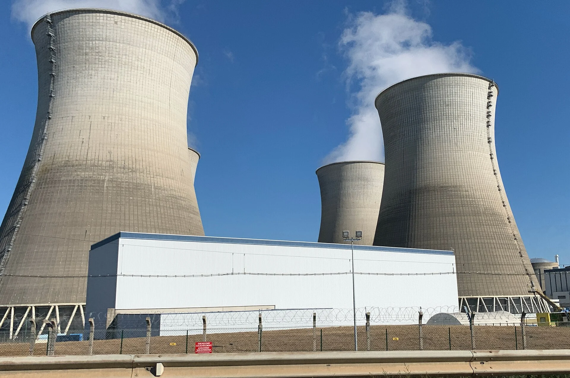 Tours de refroidissement de la centrale nucléaire du Bugey sous un ciel bleu, avec un panache de vapeur