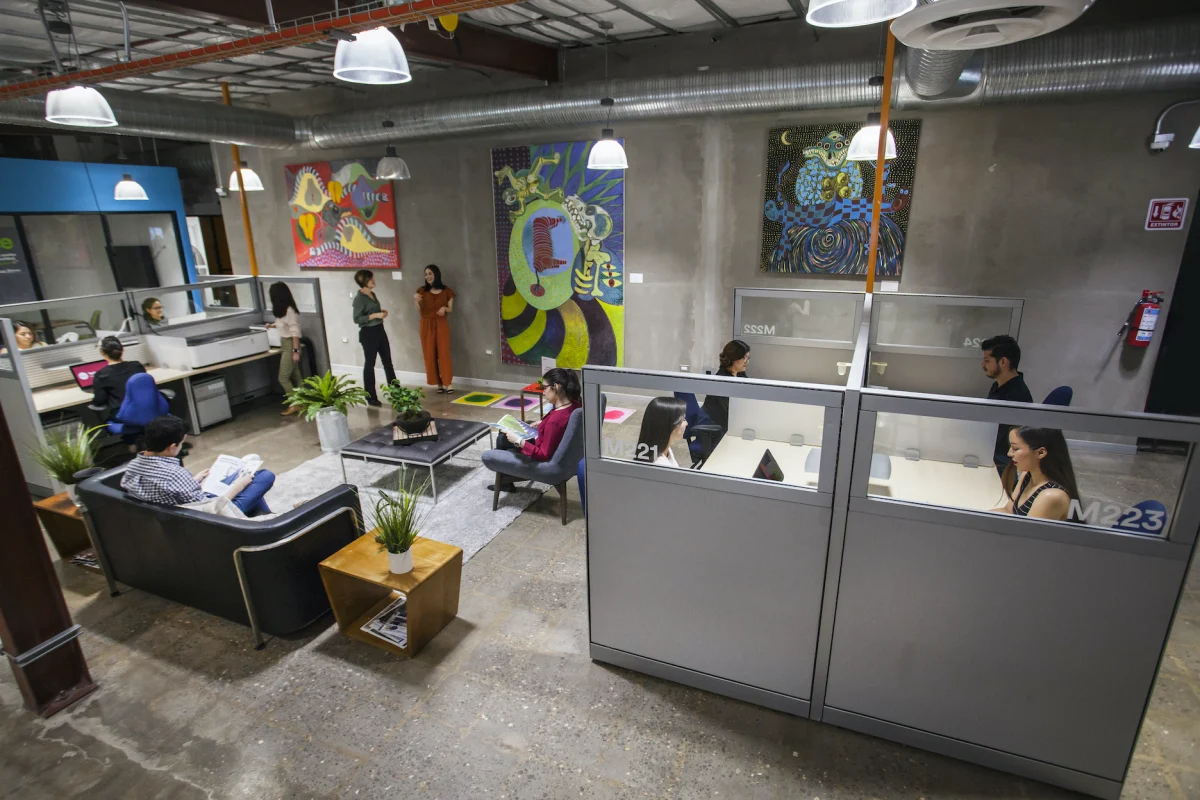 Bureaux en open space avec des salariés travaillant sur ordinateur, cloisons vitrées et salon