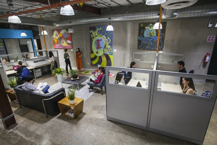 Bureaux en open space avec des salariés travaillant sur ordinateur, cloisons vitrées et salon