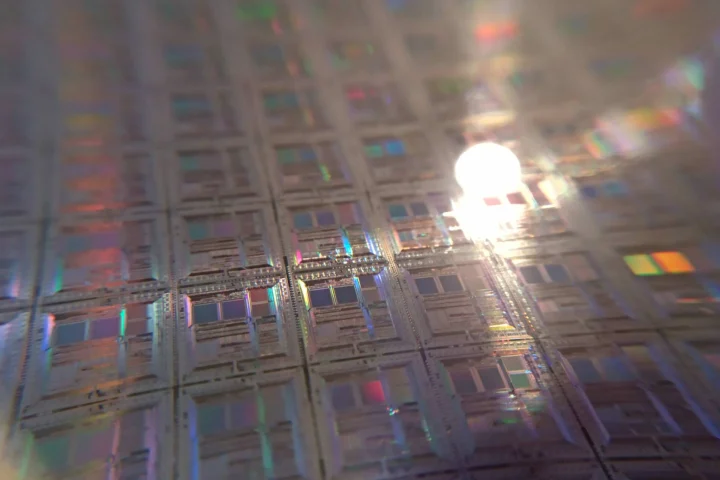 Gros plan sur une plaquette de silicium aux reflets irisés, couverte de puces identiques