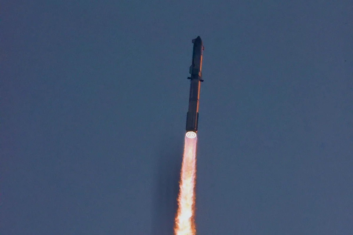 Fusée Starship en ascension dans un ciel bleu, avec une longue flamme orangée