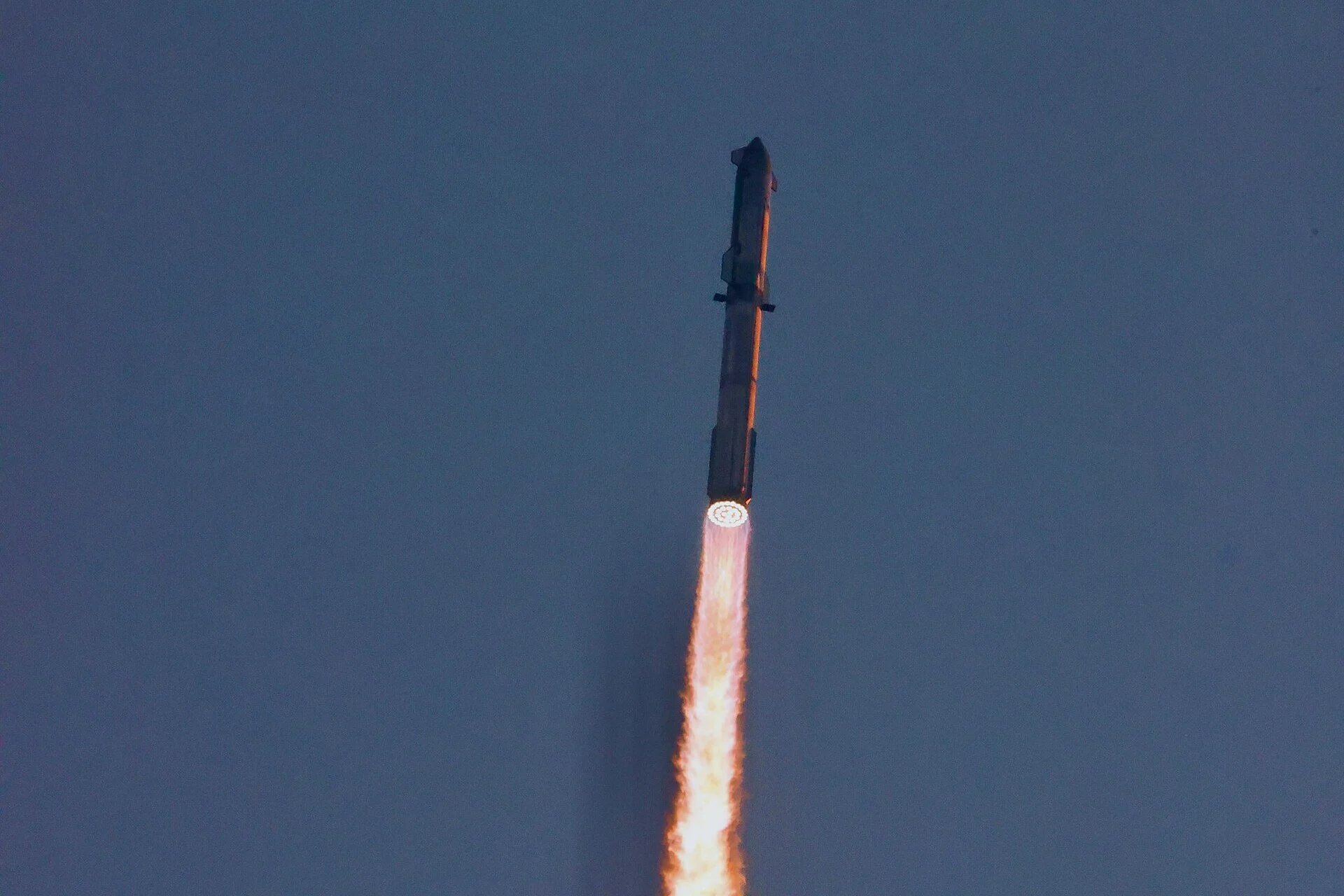 Fusée Starship en ascension dans un ciel bleu, avec une longue flamme orangée